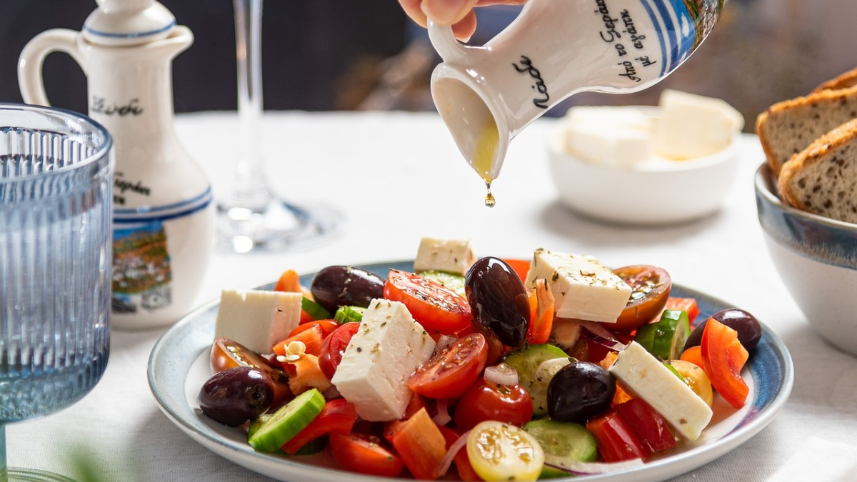 A greek salad with oil being drizzled over it