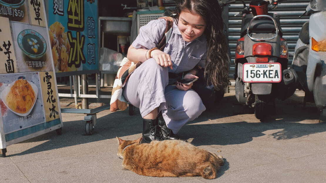 A girl kneeling next to a ginger cat in Houtong Cat Village