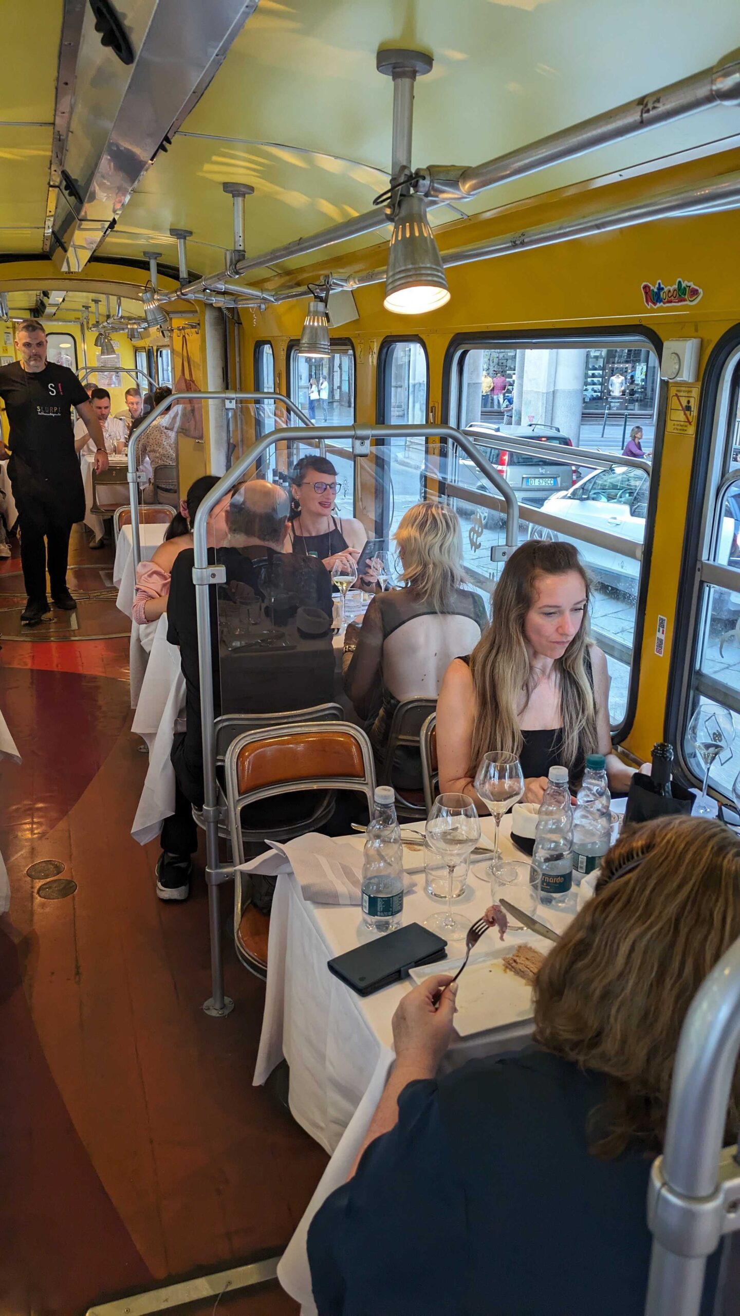 multiple tables of people eating inside the tram, the waiter walks down the centre aisle.