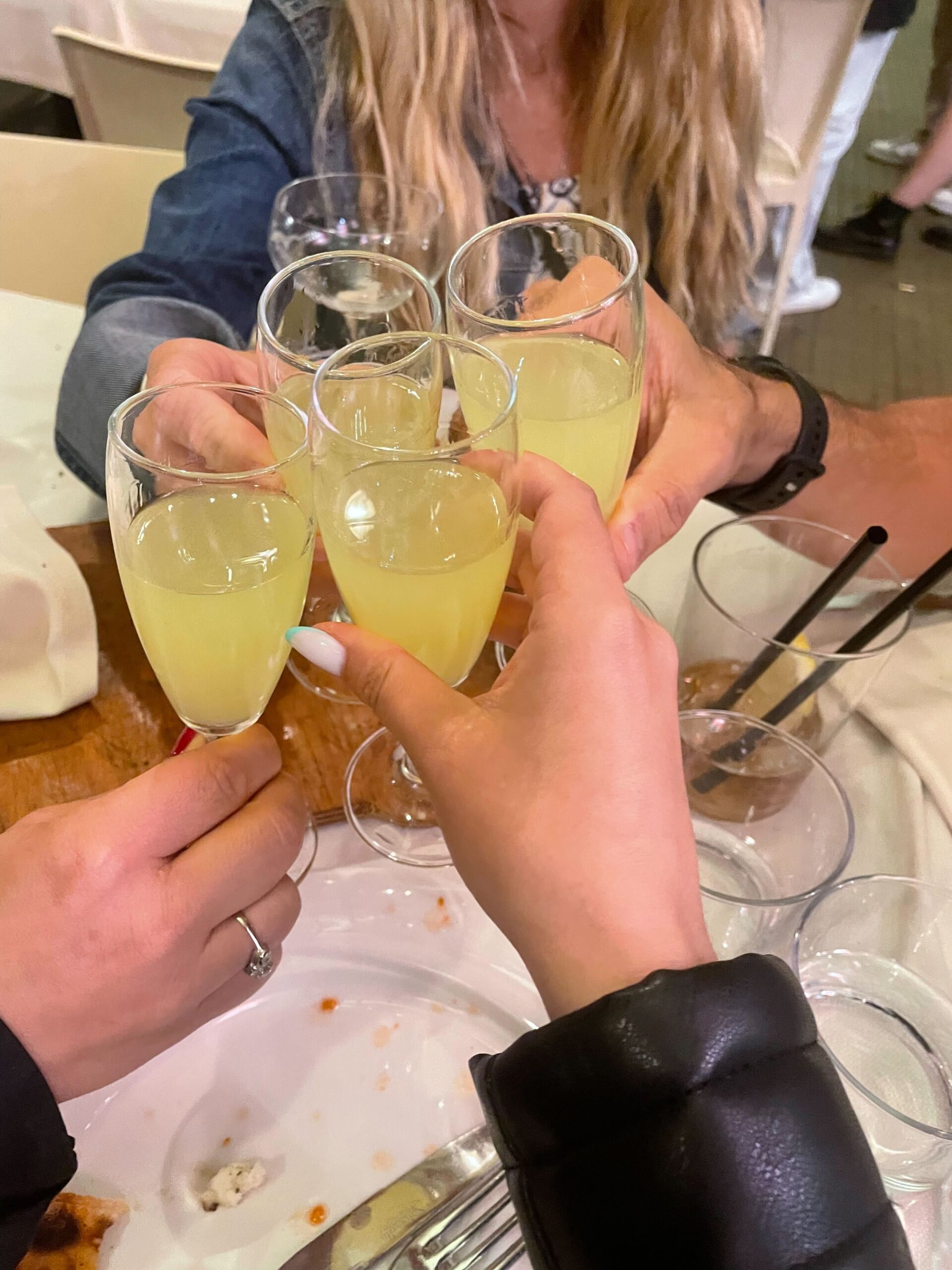Four people toasting small glasses filled with a cocktail.